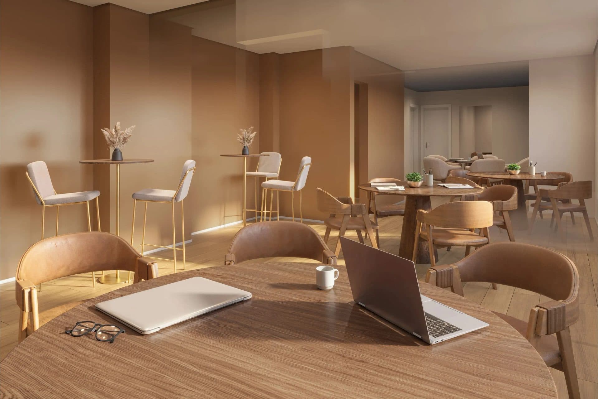 Sala de estar ou coworking com mesas redondas, cadeiras estofadas e notebooks.